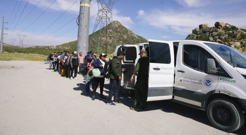 A line of migrants are processed by the US Border Patrol agents into a white van after crossing the U.S.- Mexico border.