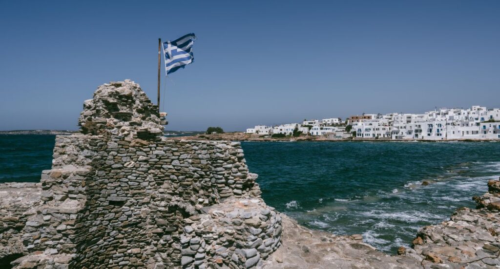 Flag of greece flies above the crumbling ruins of an old naval fort outside the city of Naousa on the island of Paros in Greece.