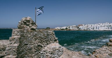 Flag of greece flies above the crumbling ruins of an old naval fort outside the city of Naousa on the island of Paros in Greece.