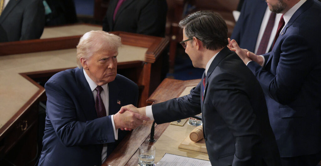 Donald Trump, in a darl blue suit, shakes hands with Mike Johnson, dressed in a dark grey suit.