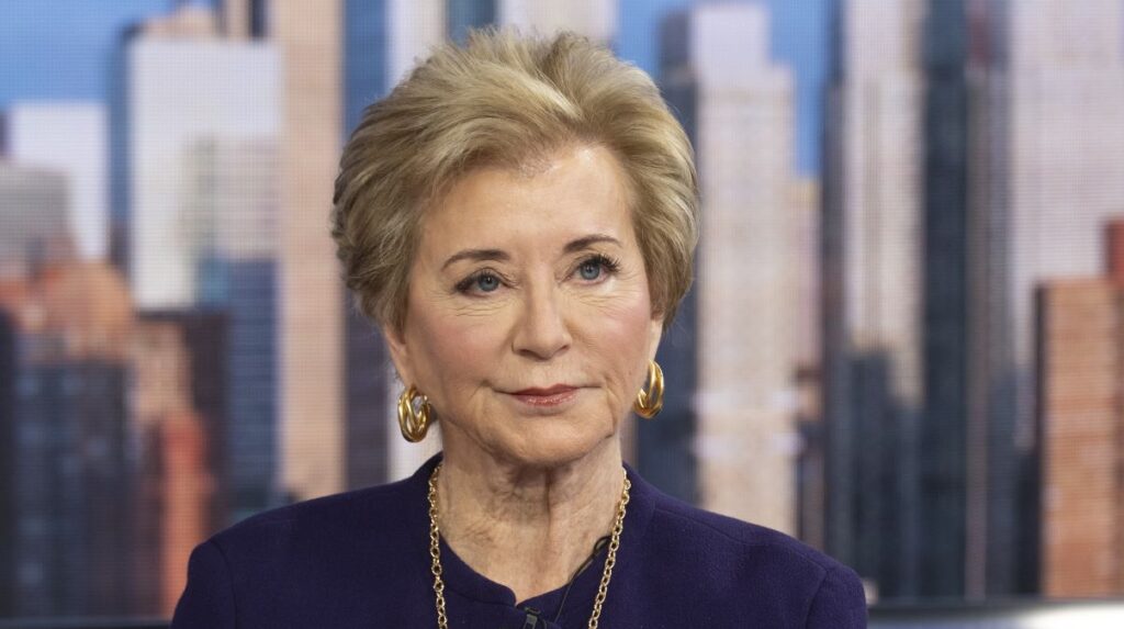Close-up of Secretary of Education Linda McMahon, in a purple jacket, with image of New York skyline in background