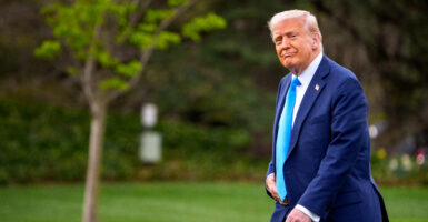 President Donald Trump in a dark blue suit and light blue tie walks outside