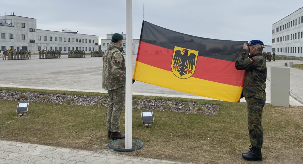A female German soldier teams with a Lithuanian soldier in preparing to raise the German flag.