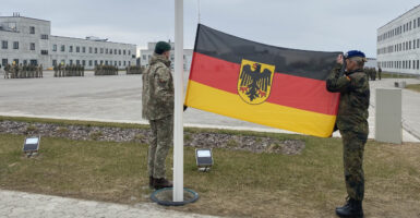 A female German soldier teams with a Lithuanian soldier in preparing to raise the German flag.