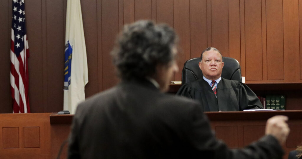 Boston Municiple Court Judge Mark Summerville looks on stoically as an ICE defense lawyer gestures toward the prosecution and argues against holding an ICE agent for "obstructing justice."