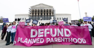 Pro-life supporters holding large "Defund Planned Parenthood" banner demonstrate in front of the Supreme Court.