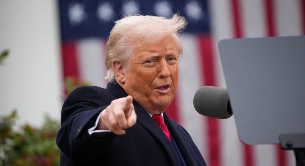 President Donald Trump pointing and speaking outside the White House in front of an American flag.