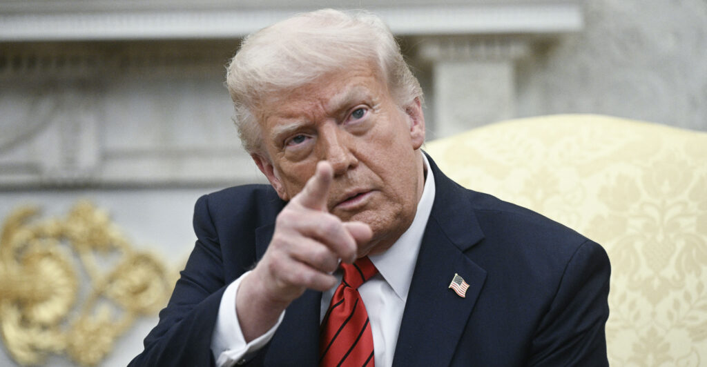 President Donald Trump points a finger while sitting in the Oval Office.
