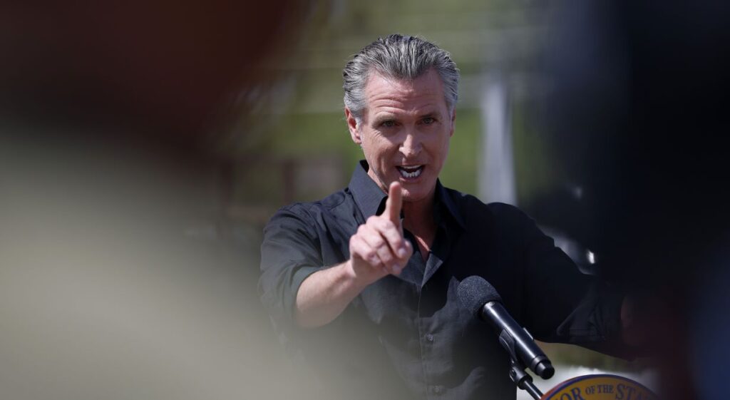 California Gov. Gavin Newsom points during and outdoor event announcing he's suing the Trump administration over tariffs.
