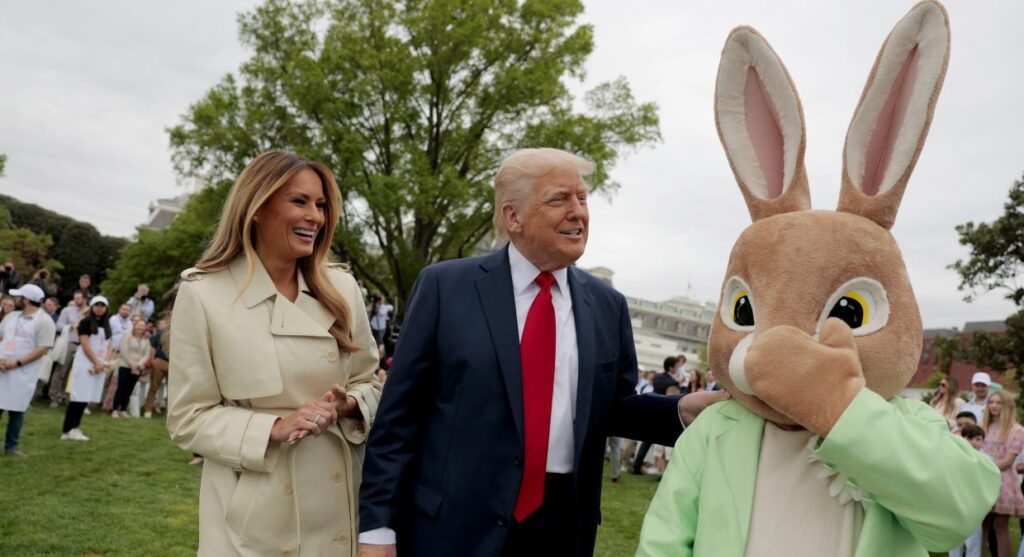 A laughing Melania Trump and the Easter Bunny flank a smiling President Donald Trump on the White House lawn during the annual White House Easter Egg Roll