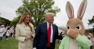 A laughing Melania Trump and the Easter Bunny flank a smiling President Donald Trump on the White House lawn during the annual White House Easter Egg Roll