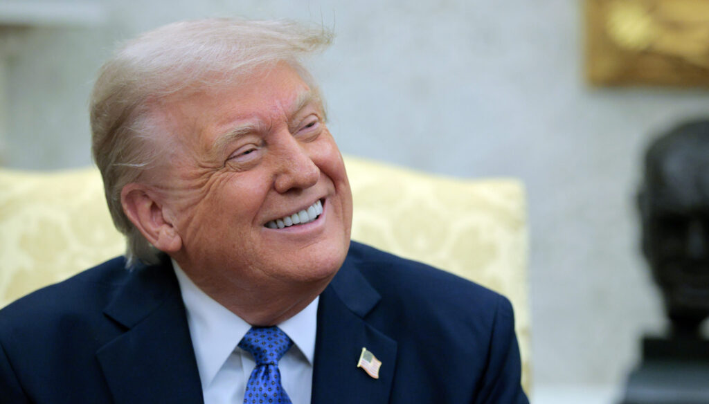 Close-up of a beaming President Trump looking to his left during an Oval Office meeting.