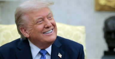 Close-up of a beaming President Trump looking to his left during an Oval Office meeting.