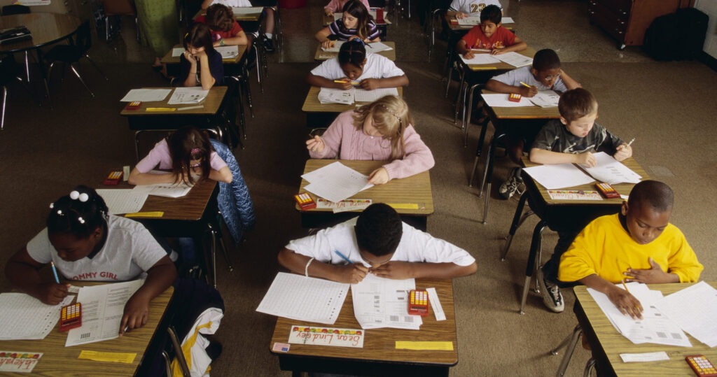 Young students about 10-12 years old sit intently at their desks taking a standardized test.