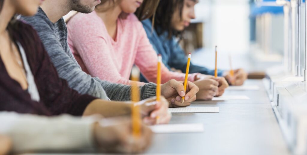 Shot down table showing five male and female high school students holding pencils take a test.