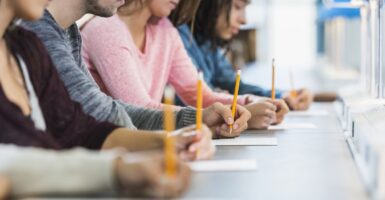 Shot down table showing five male and female high school students holding pencils take a test.