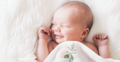 Adorable smiling newborn asleep on white blanket, while covered in a blanket with leaves and a flower.