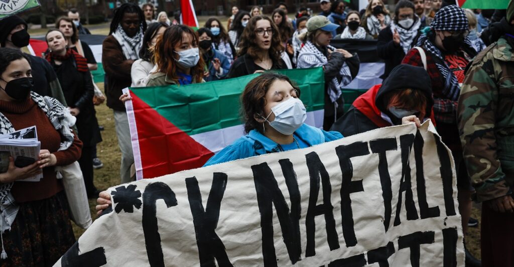 A protester at Harvard University holds an anti-Israel sign with a profanity as she marches down a street.