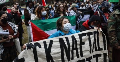 A protester at Harvard University holds an anti-Israel sign with a profanity as she marches down a street.