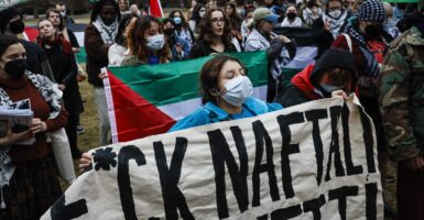 A college-aged woman holds up a sign with a profanity in it to protest a Jewish visitor to the campus of Harvard University.