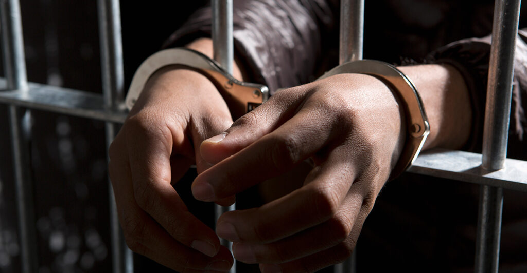 Two hands protruding from prison cell bars