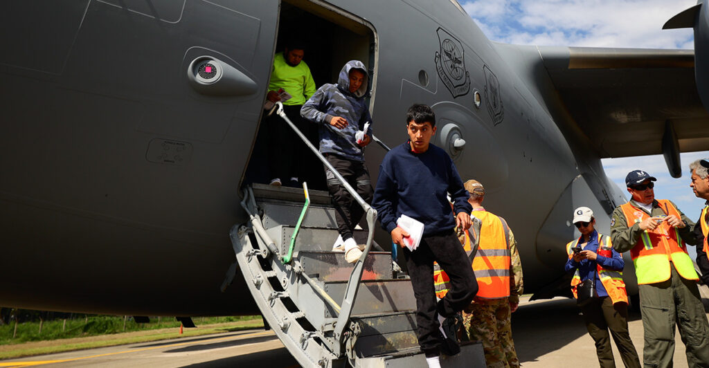 Three deported young male illegal aliens deboard a gray plane after arriving in Honduras.