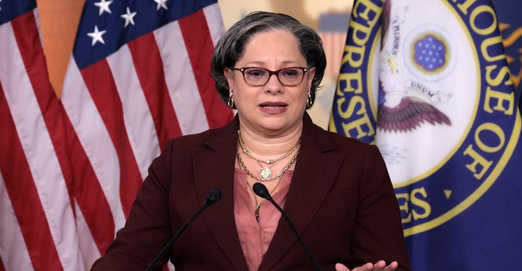 Jennifer McClellan stands in front of a podium and speaks while putting her left hand on the podium.