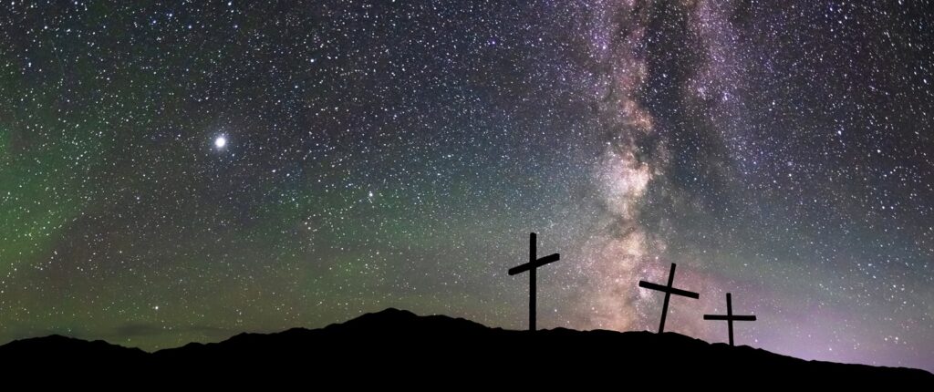 Three crosses stand on a hilltop with the stars in the background.