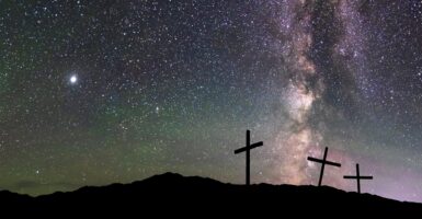 Three crosses stand on a hilltop with the stars in the background.