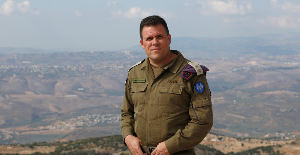 Jonathan Conricus, then spokesman for the Israel Defense Forces, stands on a mountaintop in his military uniform.