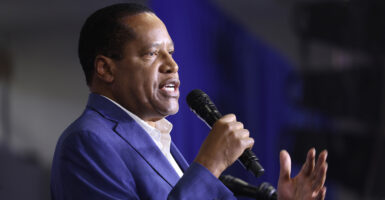 Larry Elder in a blue suit holds a microphone