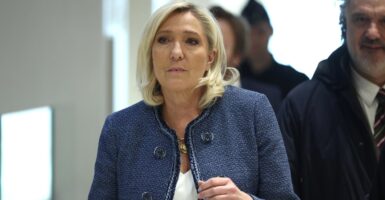 Marine Le Pen walks down a hallway while looking straight ahead.