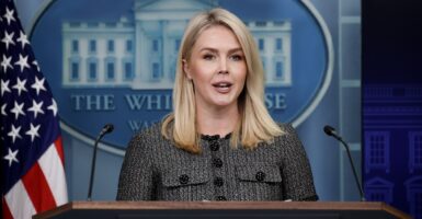 Karoline Leavitt stands behind a podium and looks straight ahead as she answers a question.