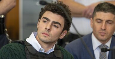 Luigi Mangione sits in court wearing a bulletproof vest as he looks to his right.