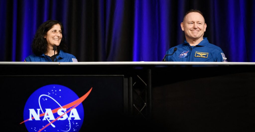 Butch Wilmore smiles as he sits at a table with fellow astronaut Suni Williams to his right.