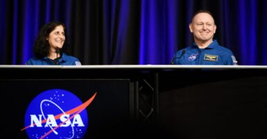 Butch Wilmore smiles as he sits at a table with fellow astronaut Suni Williams to his right.