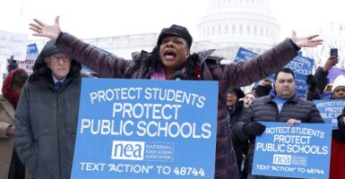 Becky Pringle stands behind a sign with both arms raised.