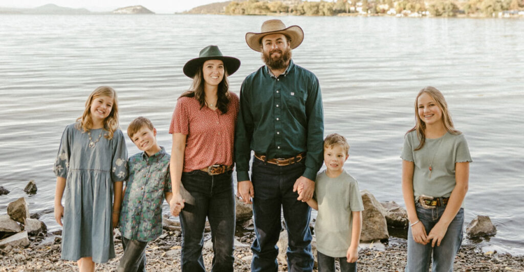 Fifth-generation farmer Rodney Cheyne with his wife in cowboy hats and their four young children standing in front of a large lake