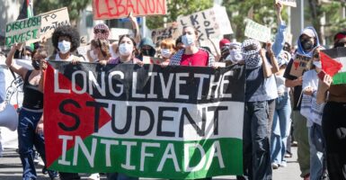 pro-Palestinian college students wearing masks walk down a street carrying a banner that calls for a student rebellion.