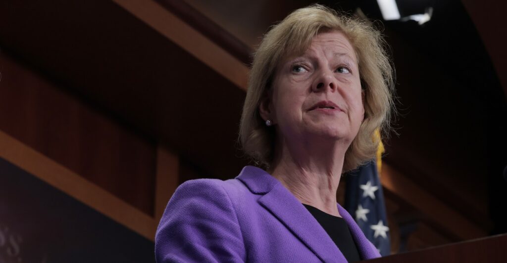 Tammy Baldwin stands at a podium and looks to her left during a news conference.