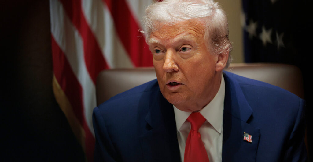 A close up of President Donald Trump speaking and looking intently during a Cabinet meeting, with an American flag behind him.