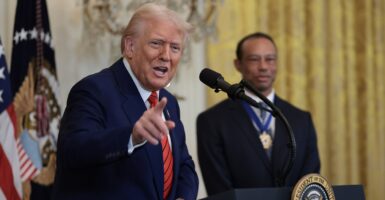 Donald Trump stands at a podium with a microphone in front of him as he talks and points with his right hand.