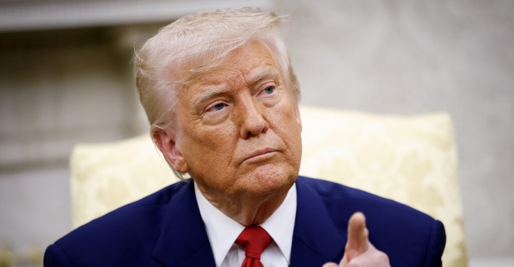 Donald Trump points with his left hand as he listens to media members.
