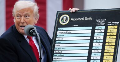 Donald Trump stands while holding a board that lists the tariffs on countries.