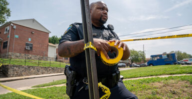 A black uniformed Baltimore Police officer hangs police tape at the site of a mass shooting