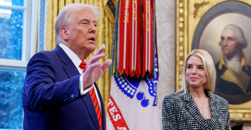 President Donald Trump in a blue suit and red tie gesturing with his hands while Attorney General Pam Bondi smiles and looks on. In the oval office.