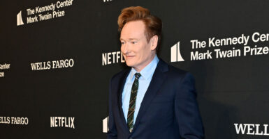 Conan O'Brien in a blue suit stands in a media photo op line