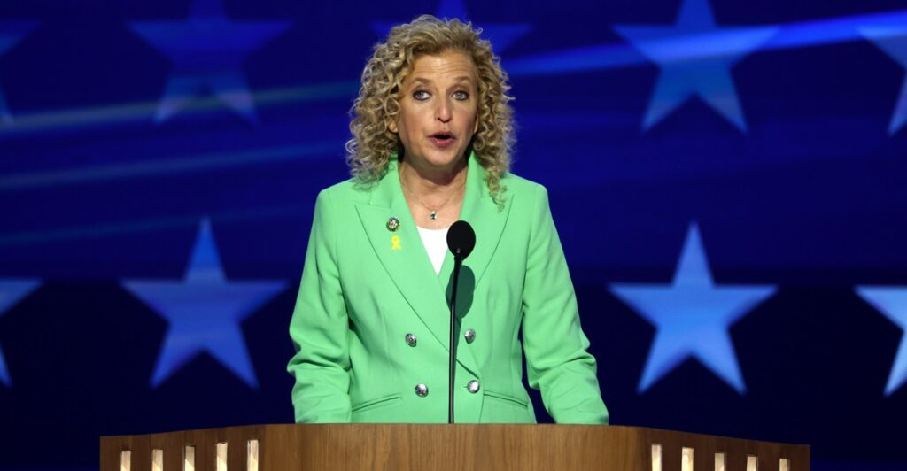 Debbie Wasserman Schultz stands at a podium in front of a microphone as she speaks at a conference.