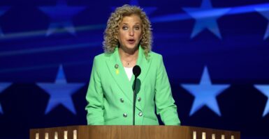 Debbie Wasserman Schultz stands at a podium in front of a microphone as she speaks at a conference.