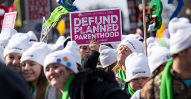 Protestors at the 2025 March for Life in white winter hats holding up Defund Planned Parenthood signs.